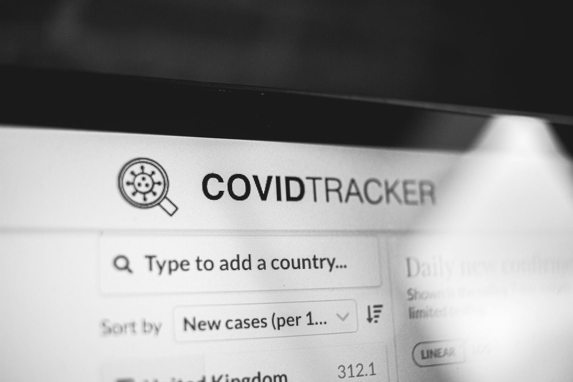 Black and white image showing COVID-19 tracker on a laptop screen with search options.