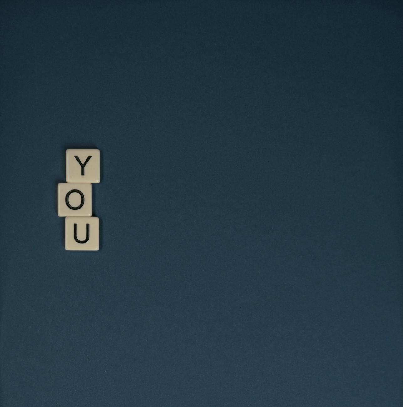 Scrabble tiles spelling 'YOU' with copyspace on a dark background in a minimalist style.